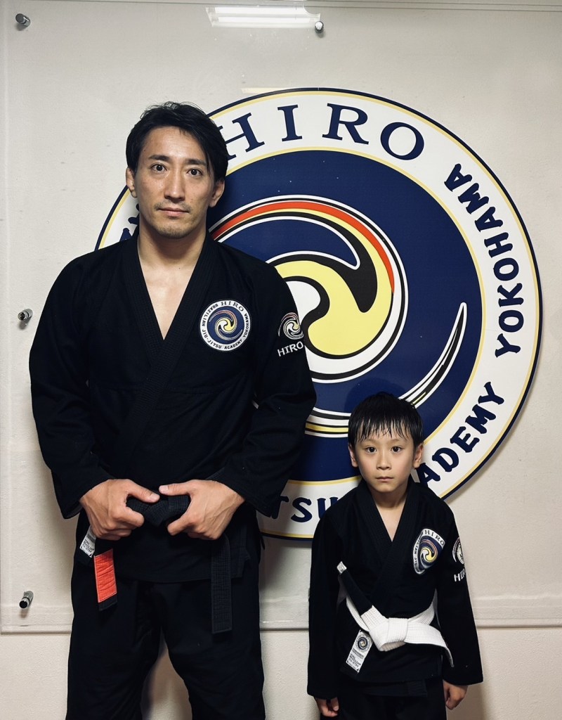 道場の前でポーズを取る二人の武道家、一人は大人の男性、もう一人は子供。